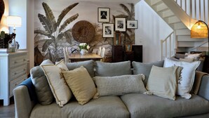 A cozy living room with a wooden ceiling, a dining table with chairs, a staircase, and a wall with framed pictures. - La Hunière Belle Maison Pour 6 Personnes (Barneville-Carteret)