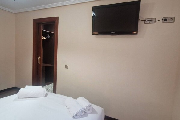 Una habitación de hotel con cama, televisión montada en la pared y un armario de madera.