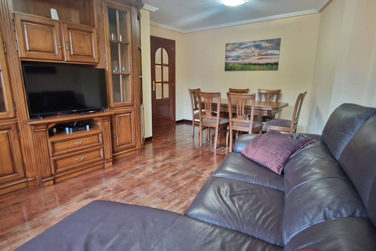 Ein Wohnzimmer mit Ledersofa, Holzschränken, einem Flachbildfernseher, einem Esstisch mit Stühlen und einem Gemälde an der Wand.