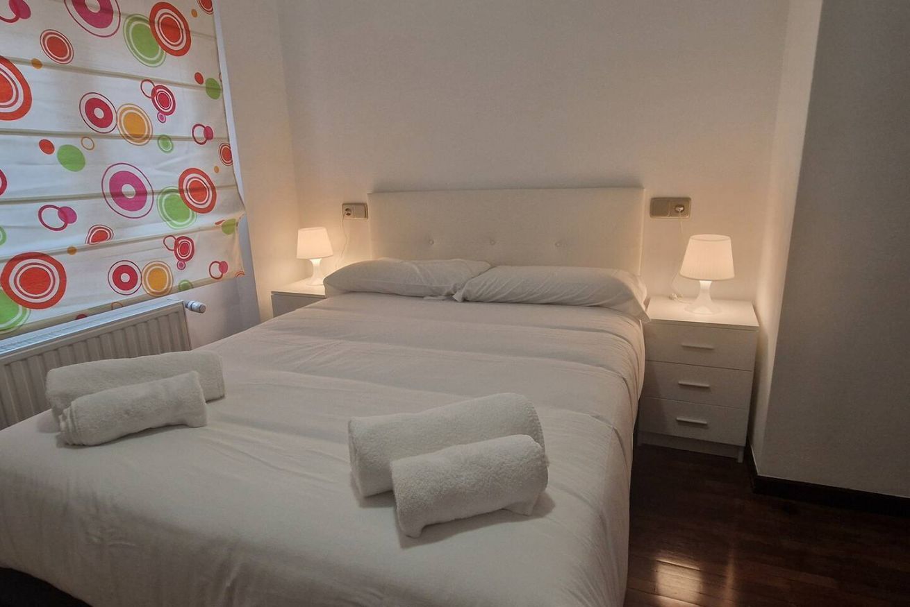 A hotel room with a large bed, two bedside tables with lamps, and a window with a colorful curtain.