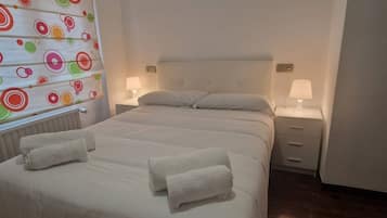 Habitación de hotel con una cama grande, dos mesitas de noche con lámparas y una ventana con cortina colorida.