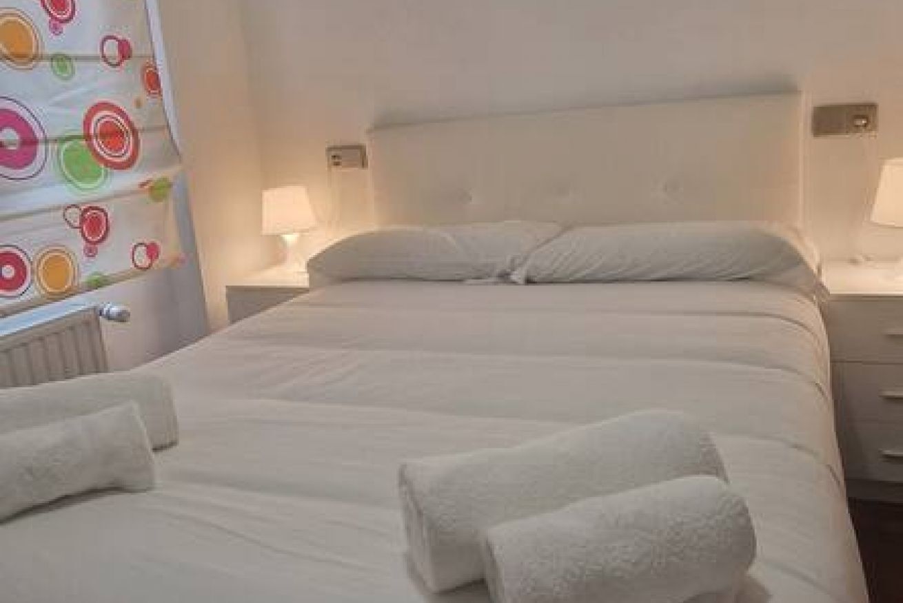Una habitación de hotel con una cama, dos mesitas de noche, una pared con un diseño circular colorido y una ventana.