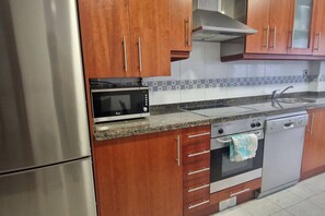 Una cocina con electrodomésticos de acero inoxidable, armarios de madera, microondas, horno y lavavajillas.