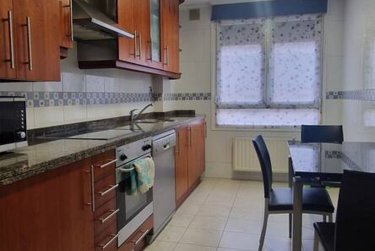Una cocina con armarios de madera, una encimera, una estufa y un ventanal con cortina estampada.