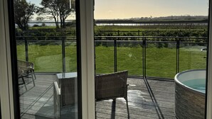 Eine Terrasse mit Whirlpool, Stühlen und Blick auf eine Rasenfläche und Bäume.