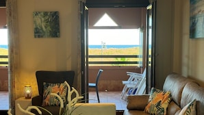 Ein Wohnzimmer mit Blick auf den Strand, eine Couch, ein Sessel und ein Tisch mit einer Lampe.