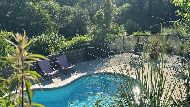 Una piscina con dos sillas reclinables, rodeada de exuberante vegetación y vistas a colinas distantes.