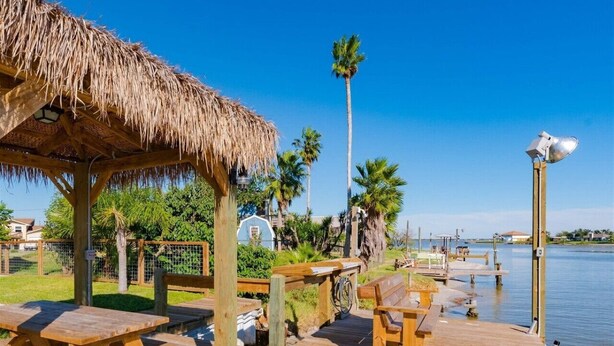 A wooden dock with picnic tables and a thatched-roof pavilion by a calm body of water.