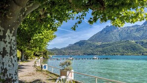 A lakeside view with a dock, boats, and a mountainous backdrop. - Rive Bleu: Charming T2 with Shared Beach (Doussard)