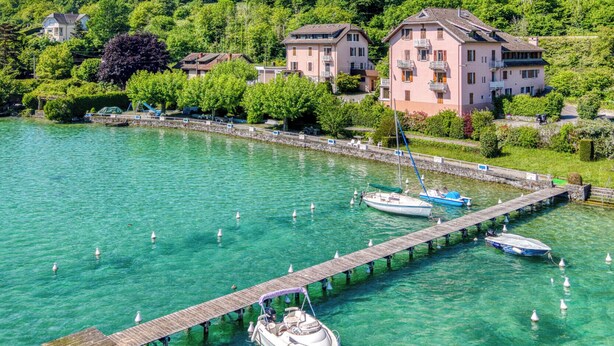 A lakeside property with a dock, boats, and a mountain backdrop. - Rive Bleu: Charming T2 with Shared Beach (Doussard)