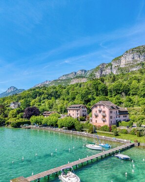 A lakeside property with a dock, boats, and a mountain backdrop. - Rive Bleu: Charming T2 with Shared Beach (Doussard)