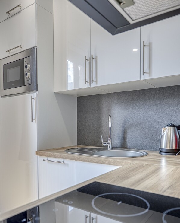 A modern kitchen with white cabinets, a stainless steel sink, a kettle, and a built-in microwave. - Rive Bleu: Charming T2 with Shared Beach (Doussard)