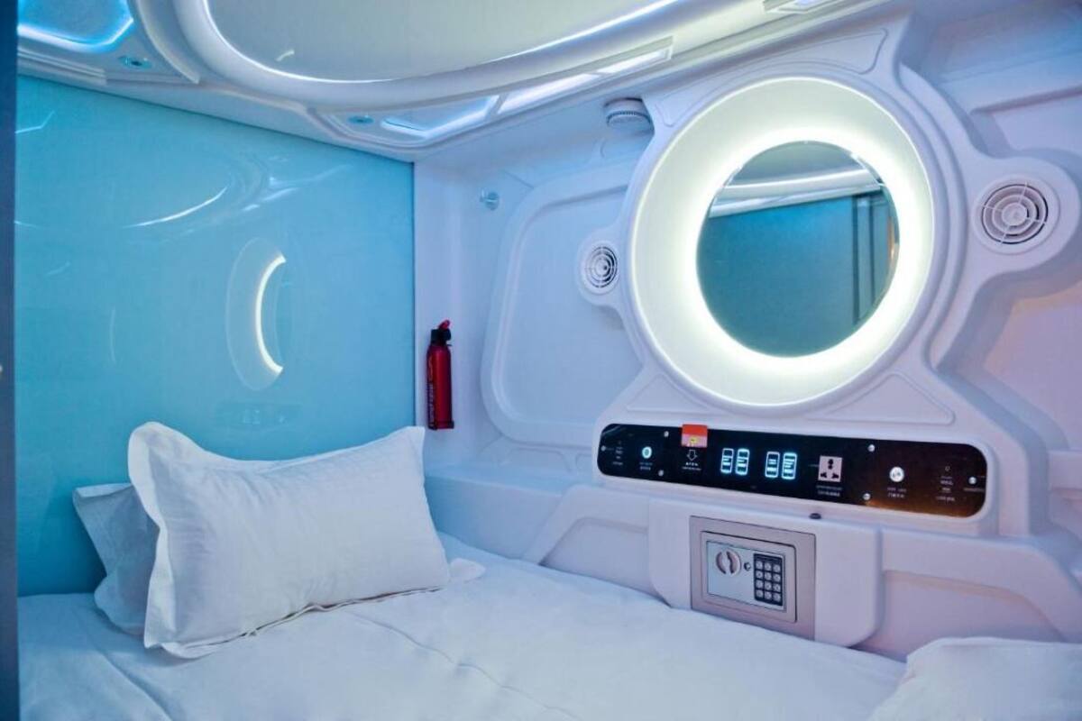 A modern, well-lit room with a bed, a control panel, and a circular window.