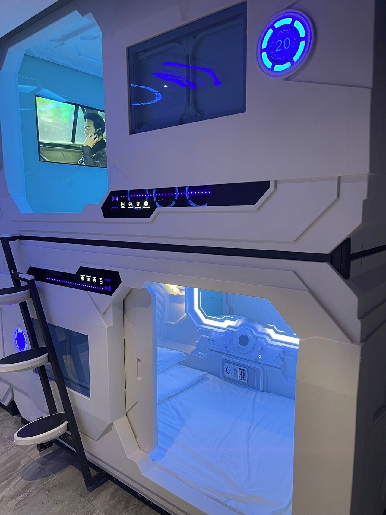 A futuristic room with a control panel, a bed, and a window displaying a cityscape.