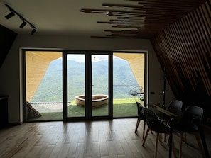 Un interior moderno con un gran ventanal corredera que da a un balcón con jacuzzi y vistas a la montaña.