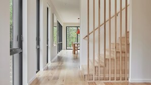 Un interior moderno con una escalera de madera, ventanas amplias y un pasillo que conduce a un comedor.