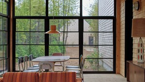 Un comedor con una mesa, sillas, ventanas amplias y una lámpara colgante.