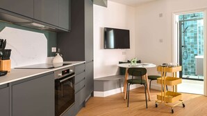 A modern kitchen with grey cabinets, a built-in oven, and a dining area with a round table and chairs. - Modern Studio in Angel | Walk to Tube | Near Regent’s Canal (London)