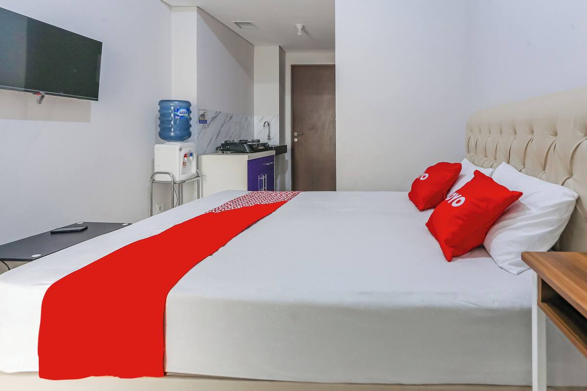 Une chambre d’hôtel équipée d’un lit, d’un téléviseur fixé au mur, d’un distributeur d’eau et d’une petite kitchenette.