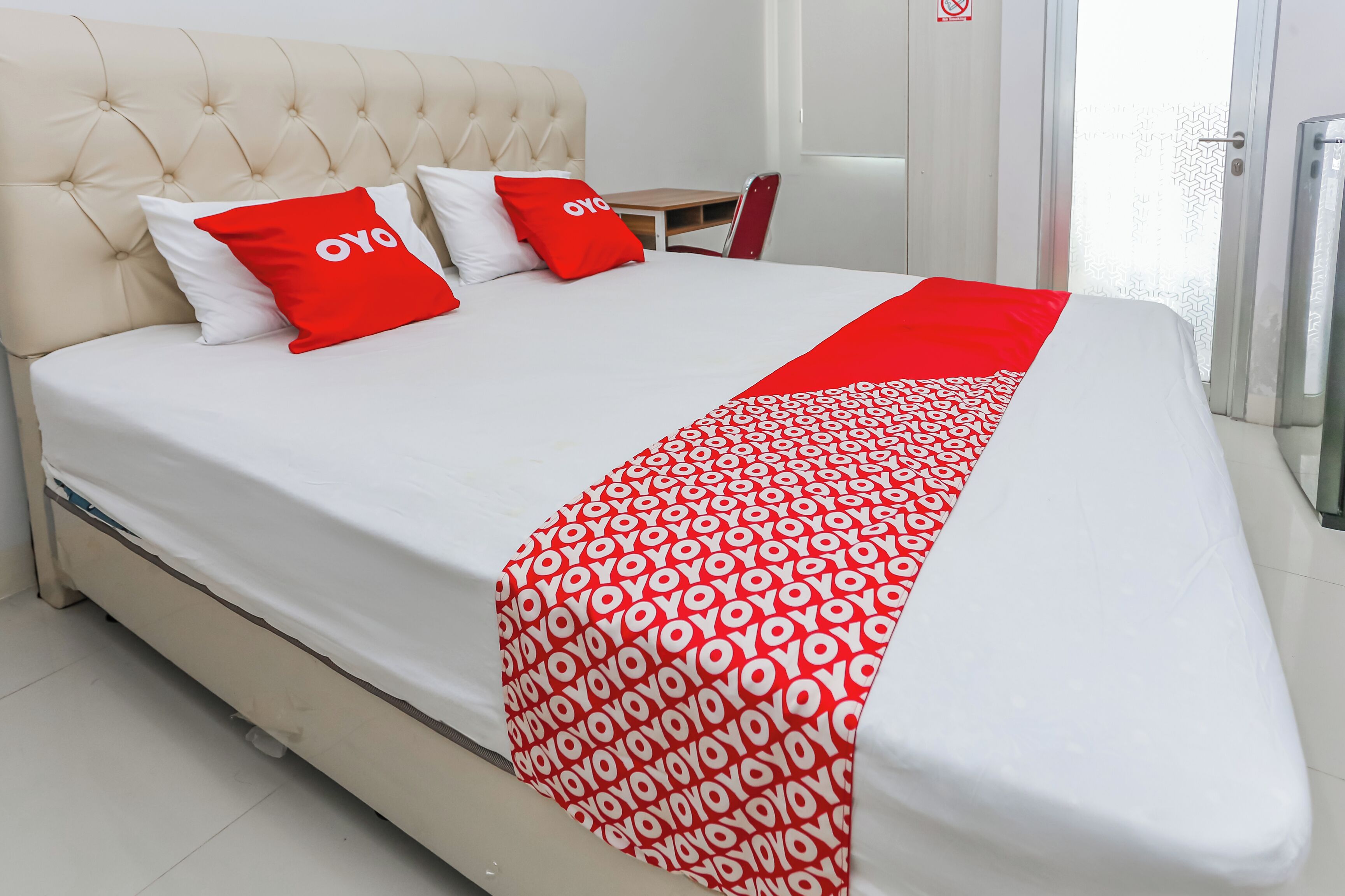 A hotel room with a large bed, a tufted headboard, and a red and white patterned throw.