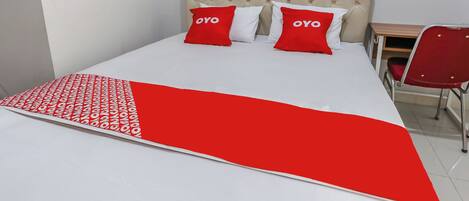 A bed with a red and white bedspread, two red pillows with "OYO" text, a tufted headboard, and a red chair next to a wooden desk.