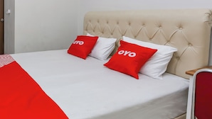 Un lit avec une tête de lit capitonnée, deux oreillers ornés du mot « OYO » et une couvre-lit rouge et blanche.