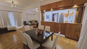 Un comedor con mesa y sillas de madera, una sala de estar con sofá y cortinas, y una cocina con armarios de madera y electrodomésticos.