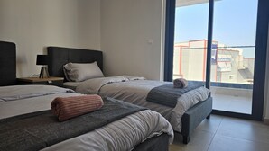 A modern hotel room with two beds, a nightstand, a lamp, and a large window offering a view of the city. - STAY Diamond Apartment (Larnaca)