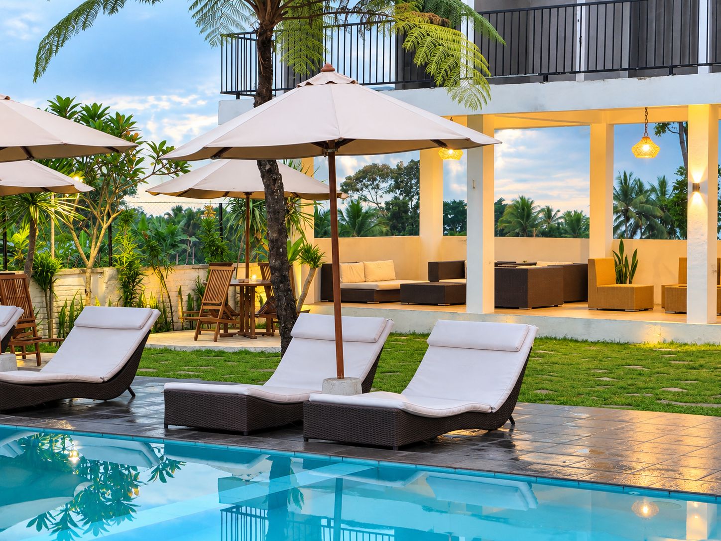Un área junto a la piscina con sillones de descanso, sombrillas y un espacio de estar con sofás y una mesa.