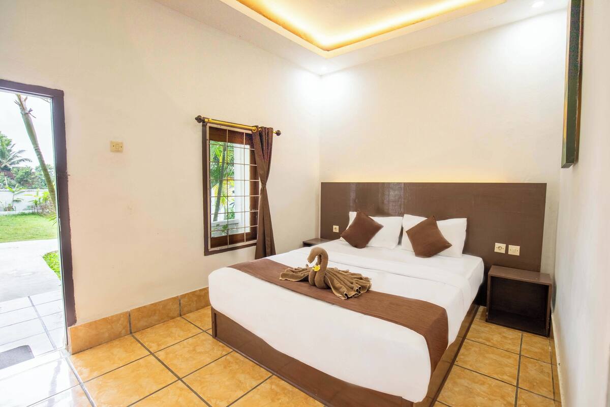 Habitación de hotel con una cama grande, una mesita de noche, una ventana con cortinas y vistas al exterior.
