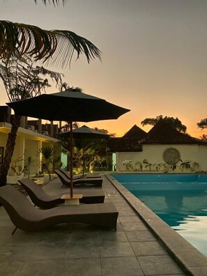 A poolside area with lounge chairs and umbrellas, a clear pool, and a building with a thatched roof in the background. - Pondok Tetebatu Cottages and Cafe  (Tetebatu)