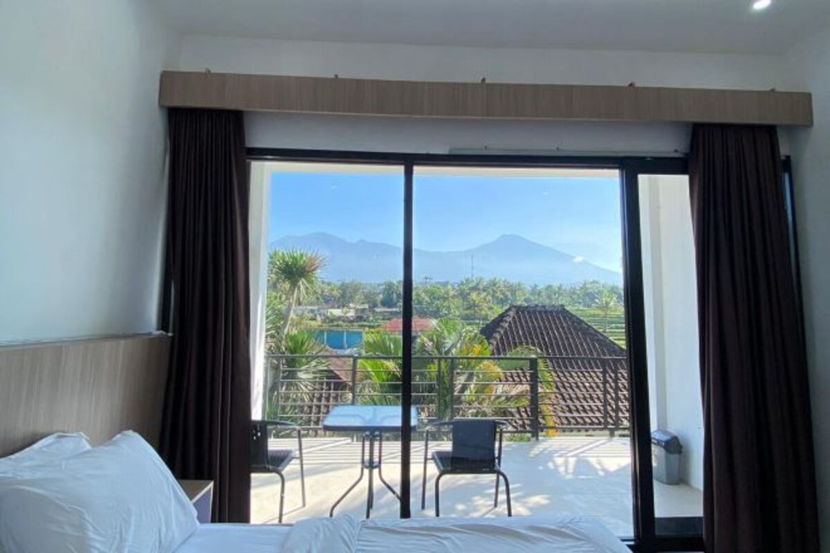 Een hotelkamer met een grote schuifglazen deur die uitkomt op een balkon met een tafel en stoelen, met uitzicht op een bergachtig landschap.