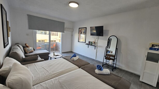 Une chambre d’hôtel avec un lit, un canapé, une petite table, une télévision et un balcon avec des chaises.