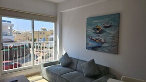 A balcony with a view of buildings and a painting of boats on the wall.