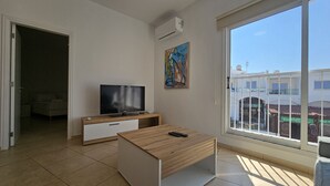 A modern living room with a flat-screen TV on a wooden stand, a small coffee table, and a large window with a view of buildings.