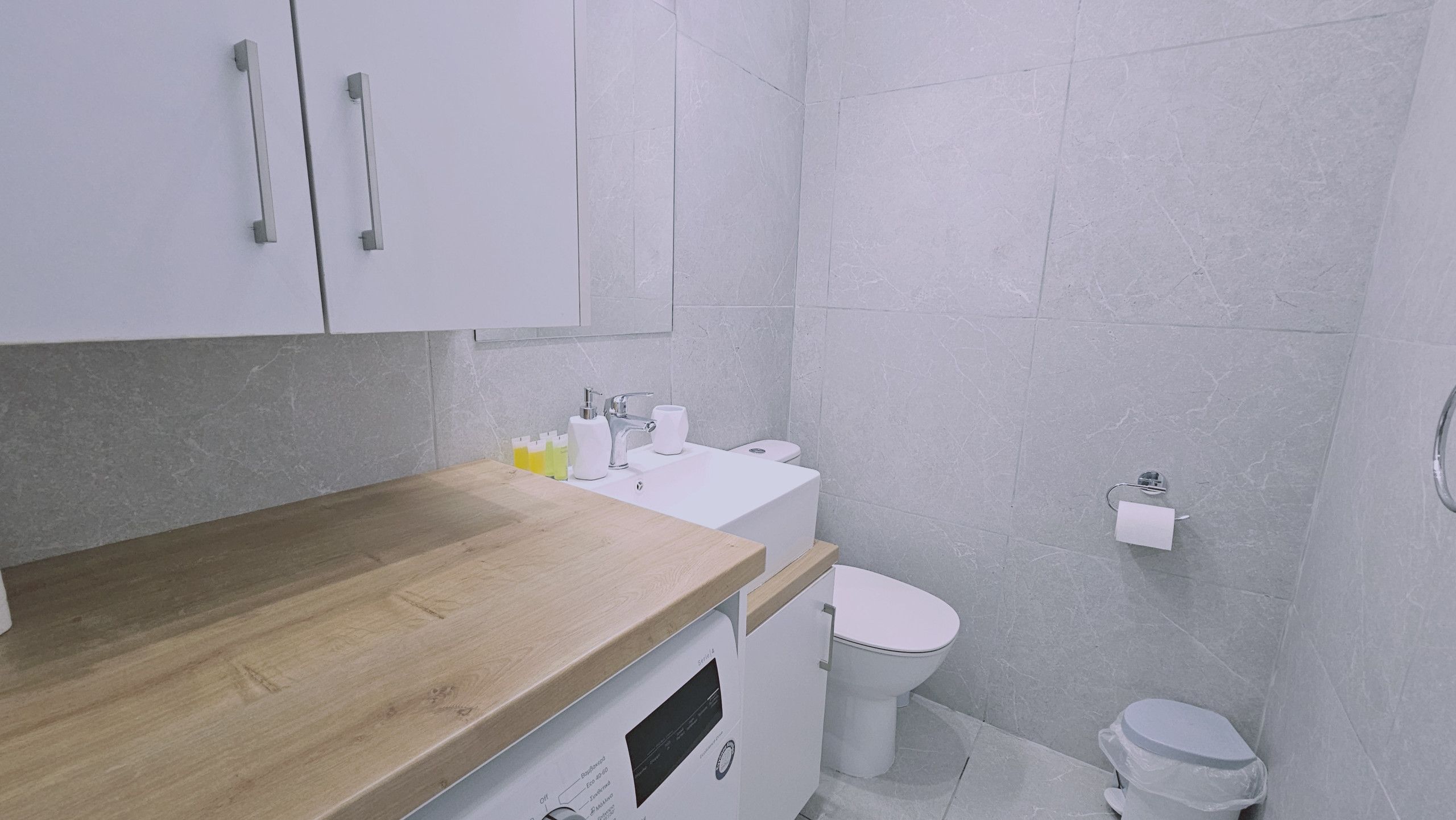 Ein modernes Badezimmer mit einer Holz-Arbeitsplatte, einem weißen Waschbecken und einer Toilette.