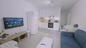 A modern living room with a flat-screen TV, a sofa, a coffee table, and a kitchen area with cabinets and appliances. - STAY Historia Apartment (Nicosia)