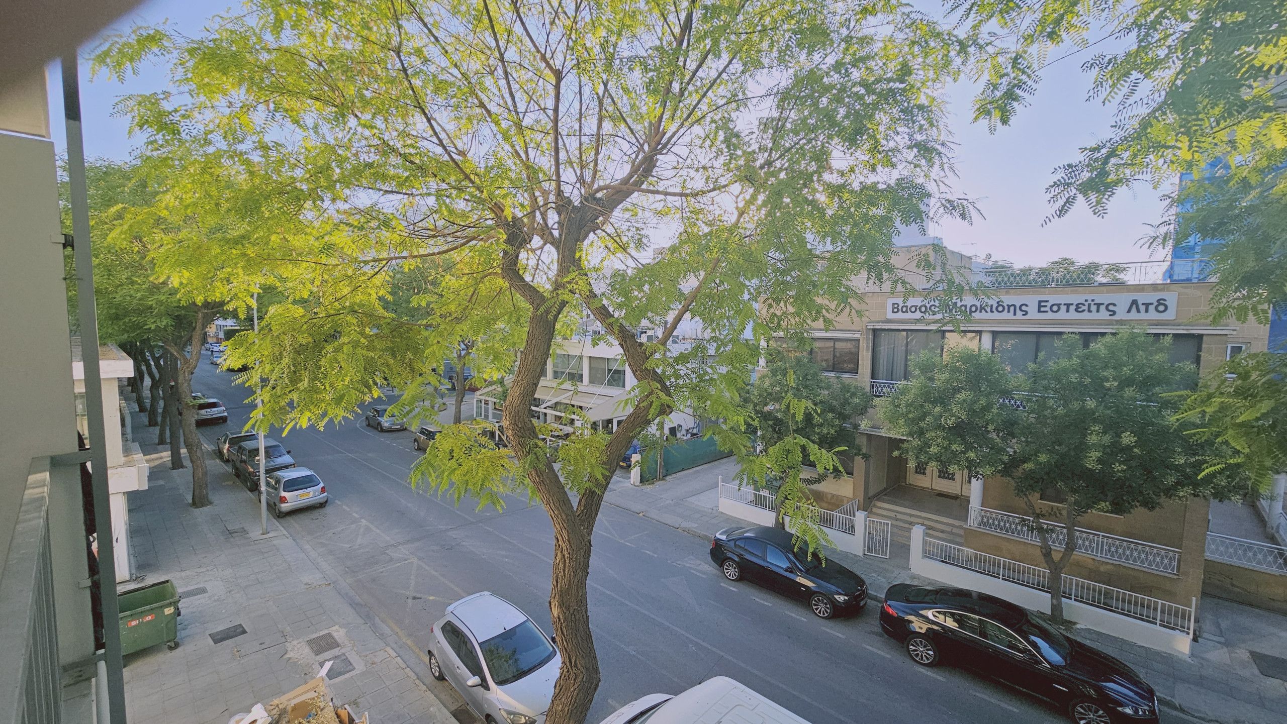 Straßenansicht mit parkenden Autos, einem Baum und einem Gebäude mit einem Schild.