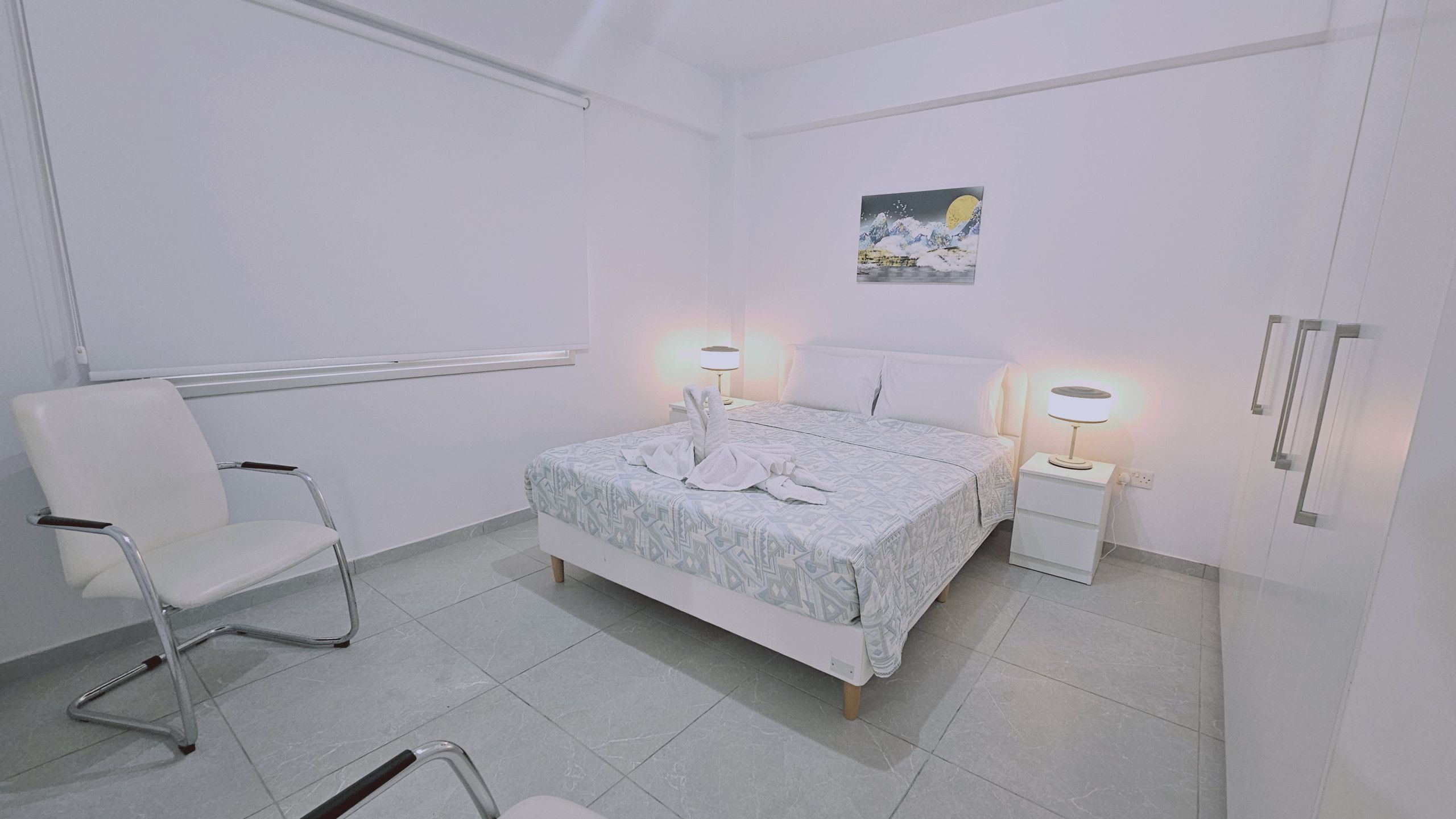 Habitació d'hotel amb un llit, una cadira, una tauleta de nit i un armari fixat a la paret.