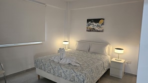 A neatly arranged bedroom with a bed, two bedside lamps, a nightstand, and a wall-mounted painting. - STAY Historia Apartment (Nicosia)