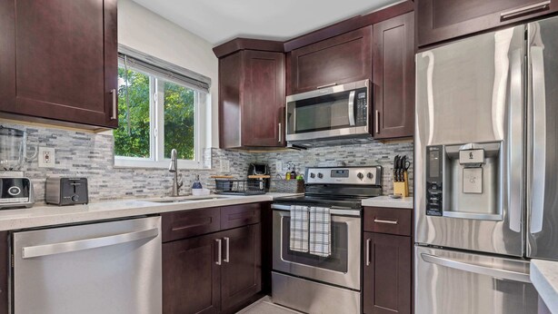 A modern kitchen with stainless steel appliances, dark wood cabinets, and a window providing natural light. - Good Vibes Sanctuary, Central Location South Miami (Cutler Bay)