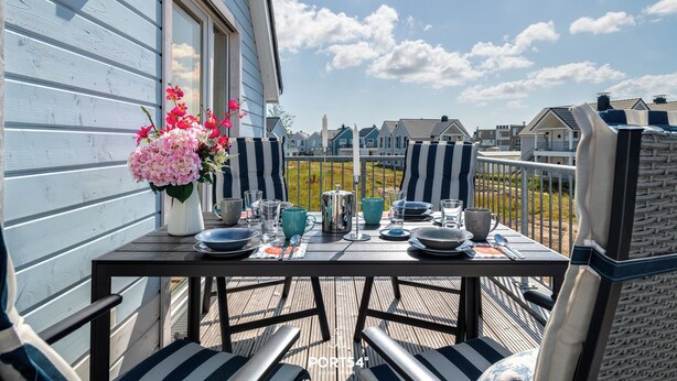 A deck with a table set for dining, chairs, and a vase of flowers.