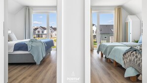 A modern bedroom with two beds, large windows, and a view of neighboring houses.