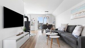 A modern living room with a flat-screen TV, a grey sofa, a coffee table, and a dining area with chairs.