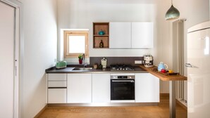 Een moderne keuken met witte kasten, een inbouwoven, een spoelbak en een houten aanrecht. Boven de spoelbak is een raam en er is een plank met decoratieve objecten.