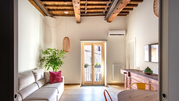 Een moderne woonkamer met een houten plafond, een bank met rode kussens, een potplant en een eethoek met een houten tafel en stoelen.