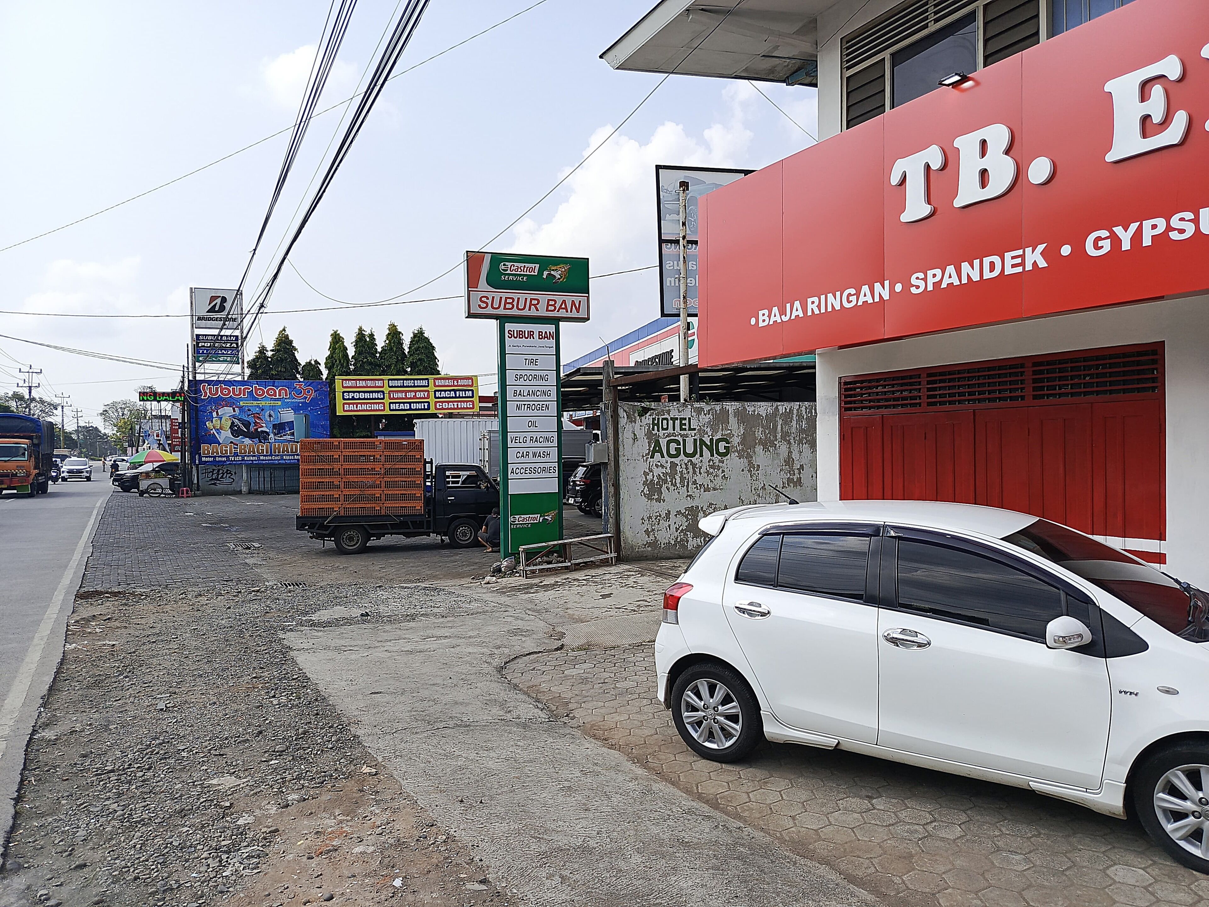 A white car parked in front of a building with a sign for 'TB. E' and 'BAJA RINGAN'.