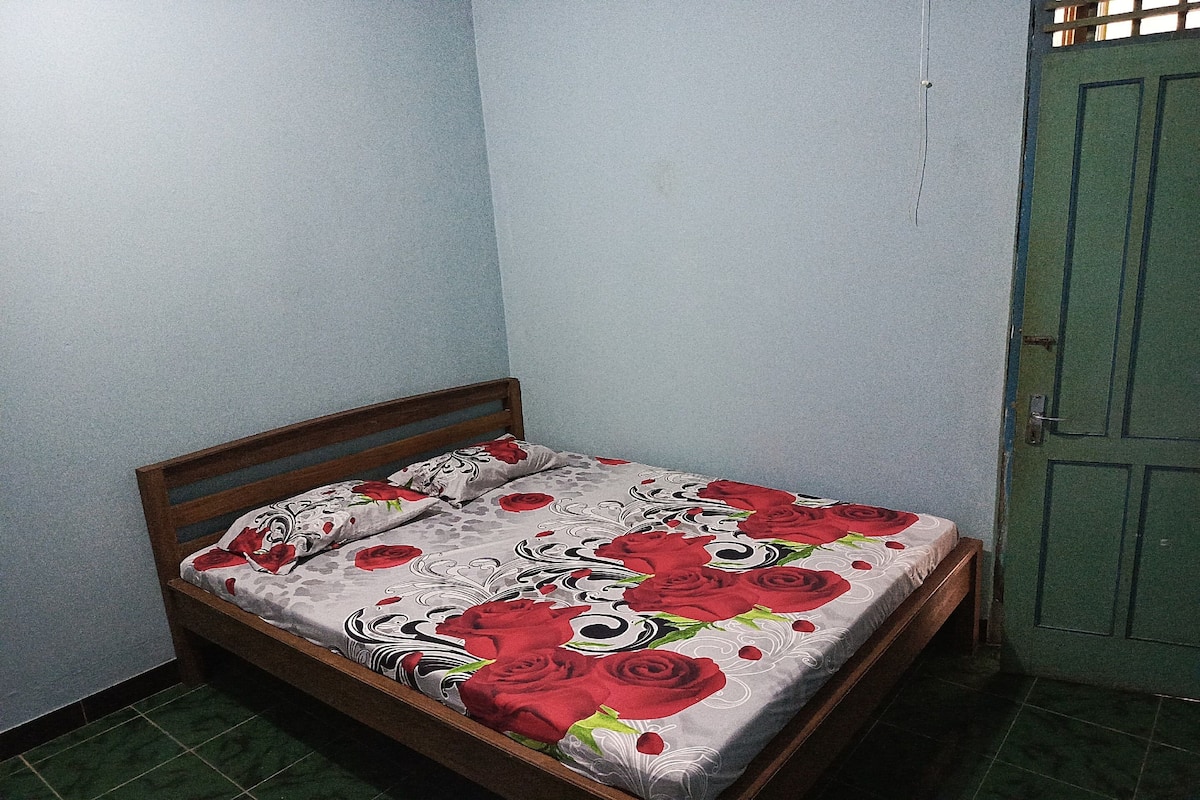Uma cama de solteiro com colcha florida num quarto com paredes azul-claras e porta verde.