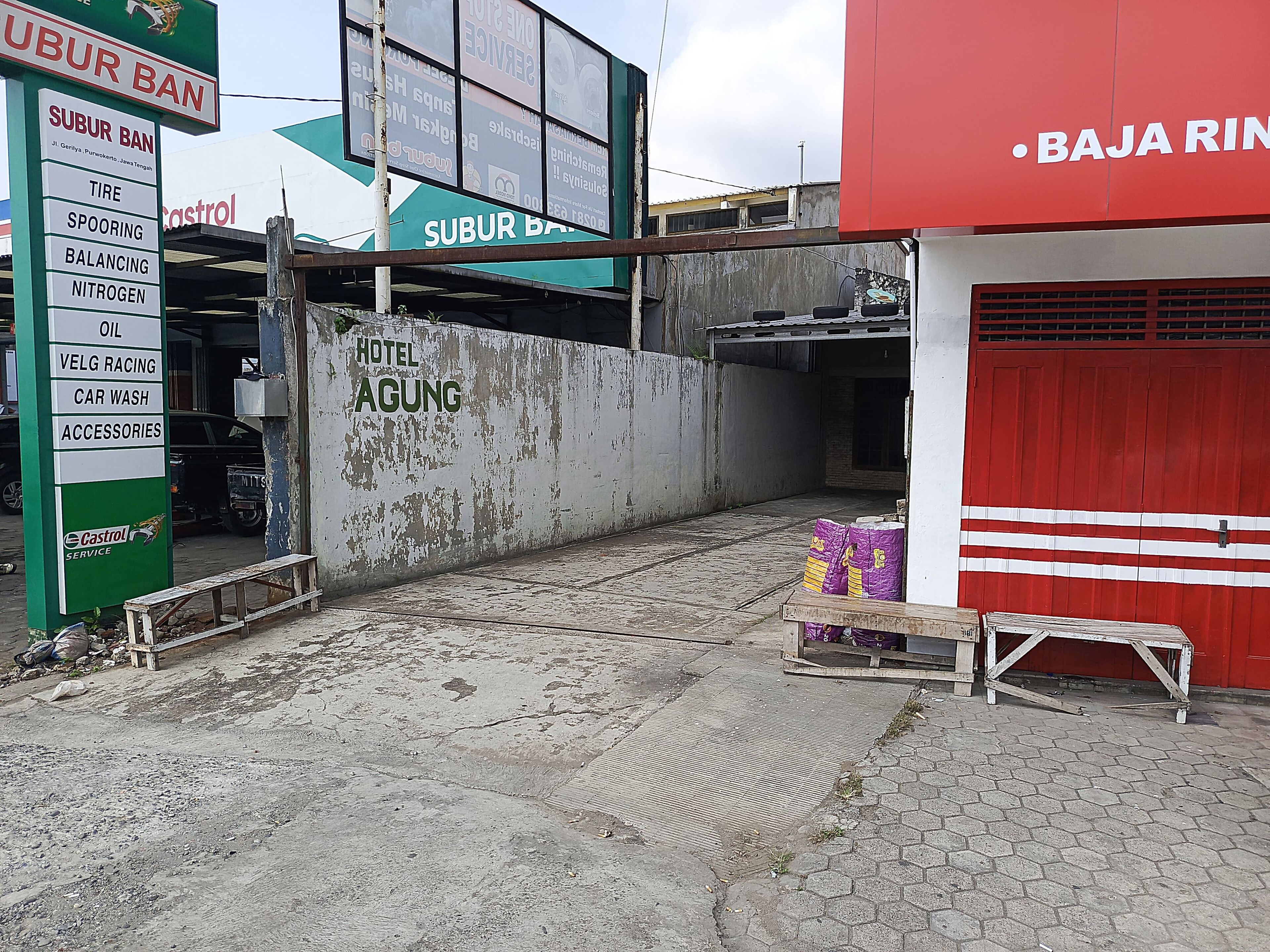 A building with a sign for 'Hotel Agung' and a 'Subur Ban' sign listing services like tire, oil, and car wash.