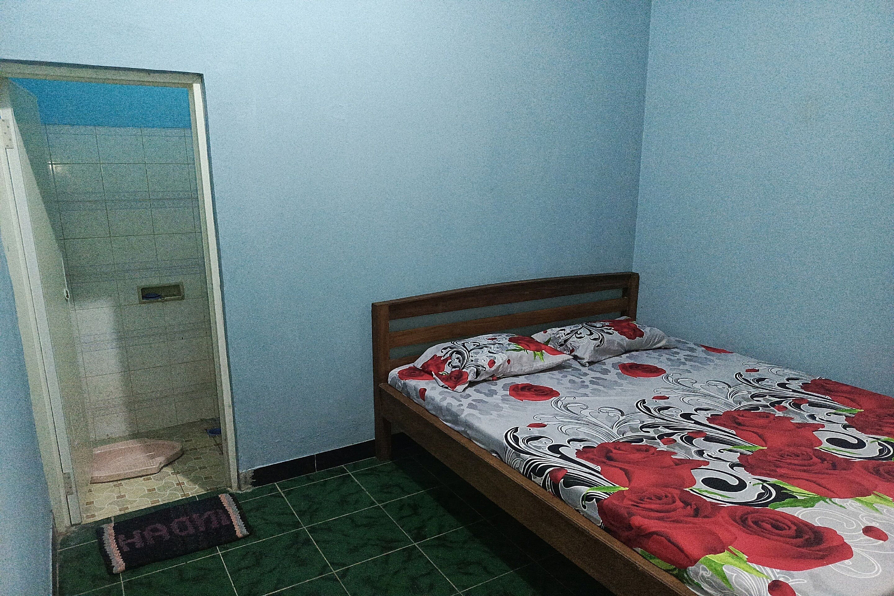 A small room with a bed, a shower, and a green tiled floor.